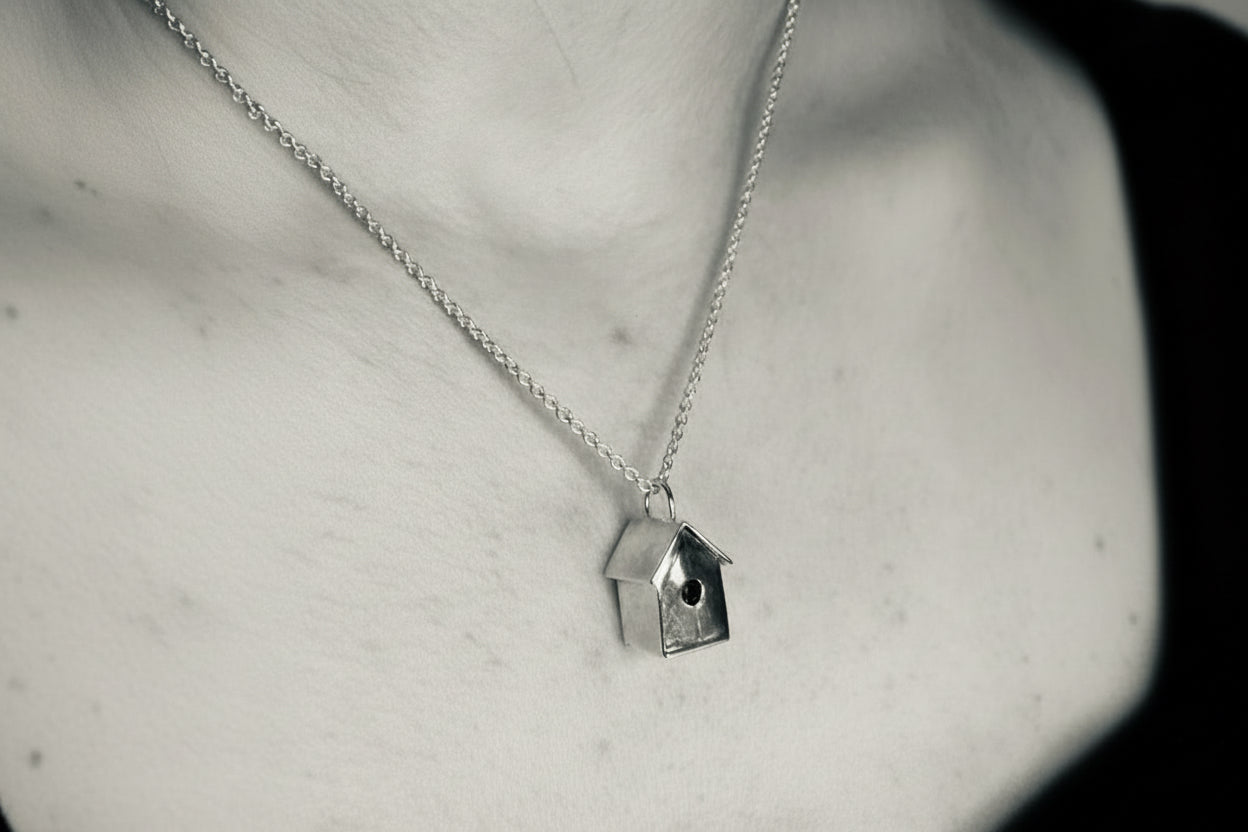 Silver necklace with a birdhouse pendant on a neutral background
