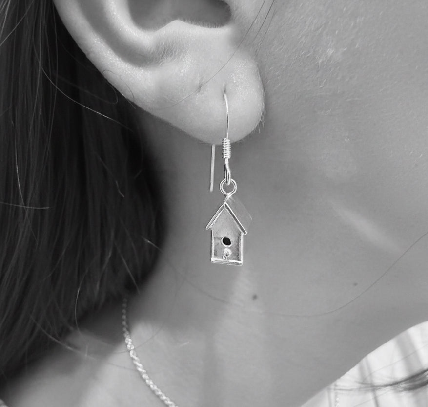 Silver birdhouse earring worn on an ear