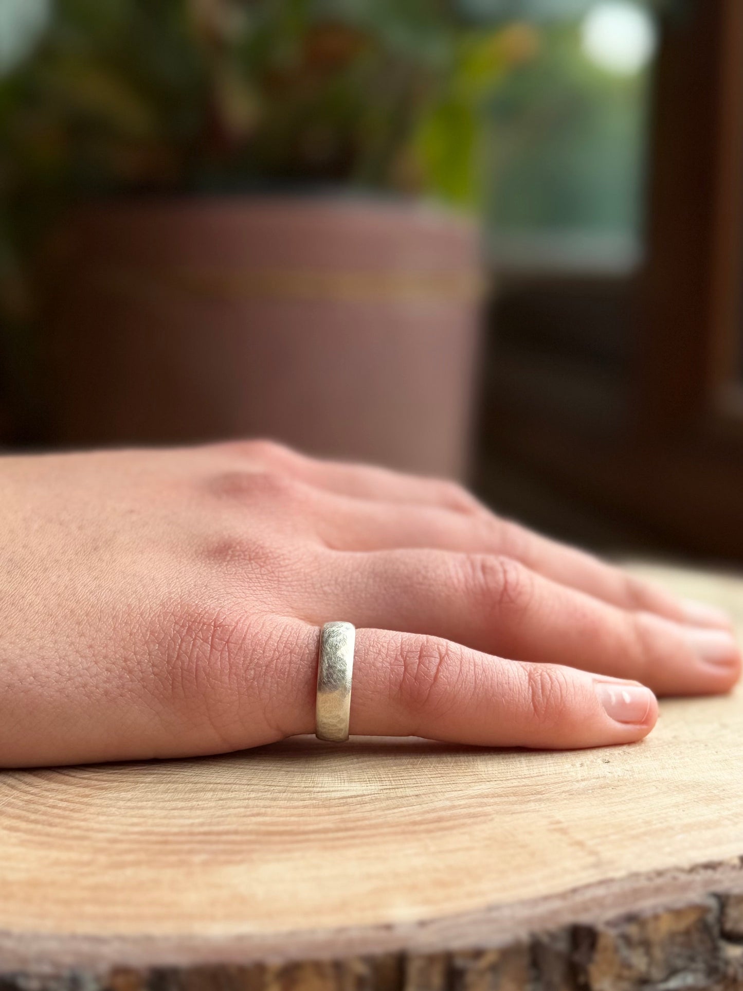 Silver hammered ring band on hand resting on wood
