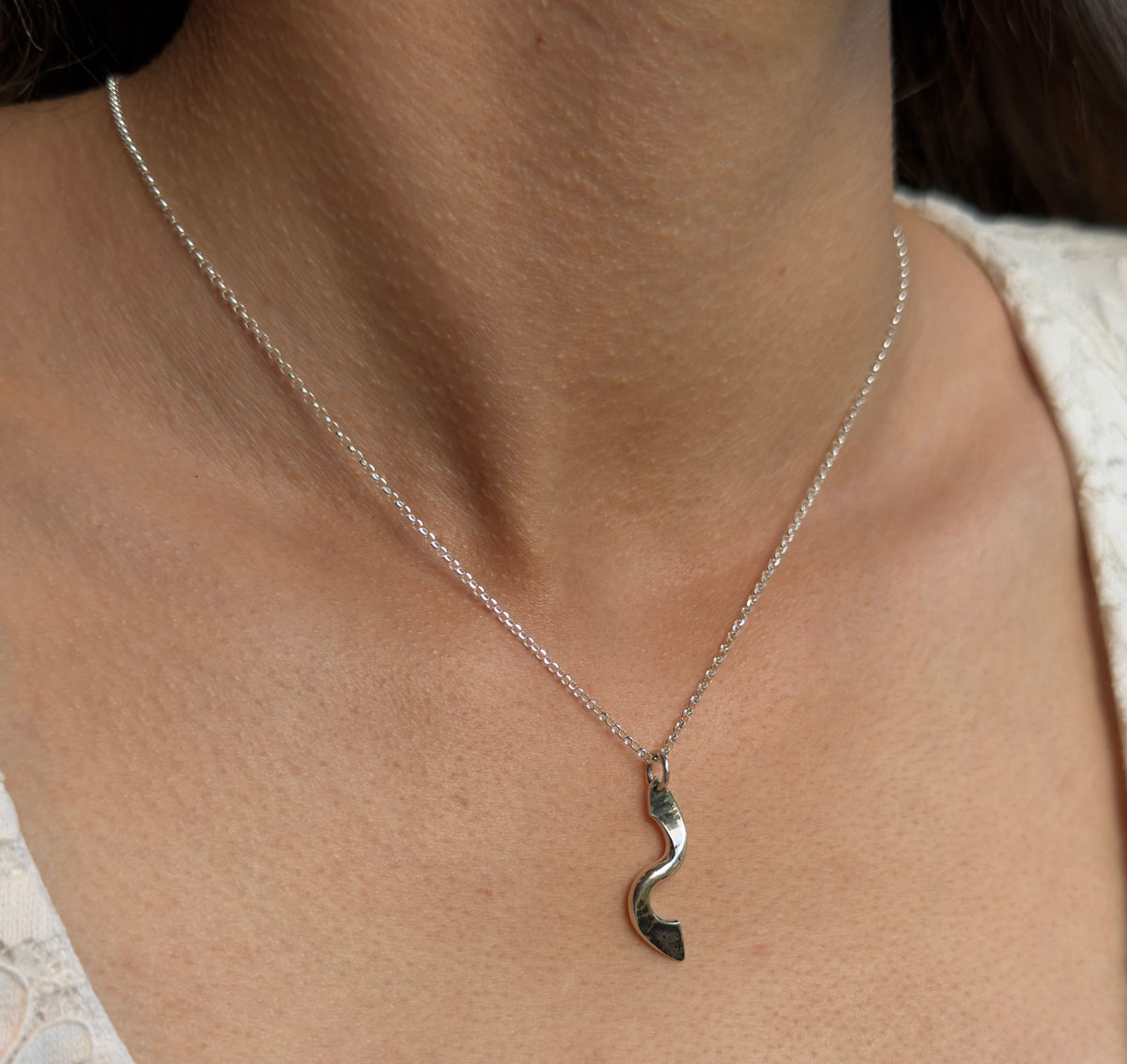 Front view of a polished silver twist pendant on a fine chain, worn against the skin with a white lace top.