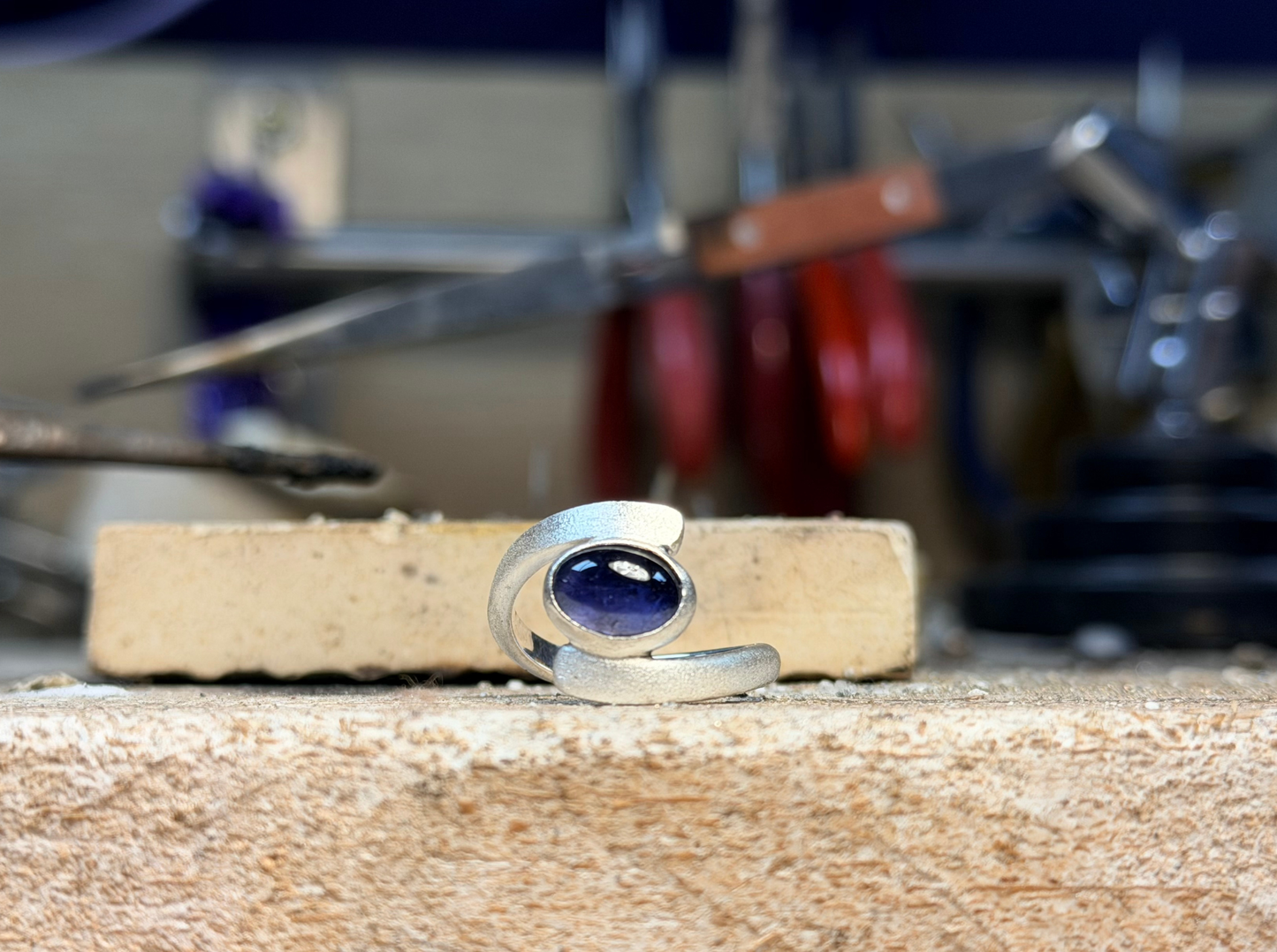 Silver ring with a purple stone on a wooden block in a workshop setting