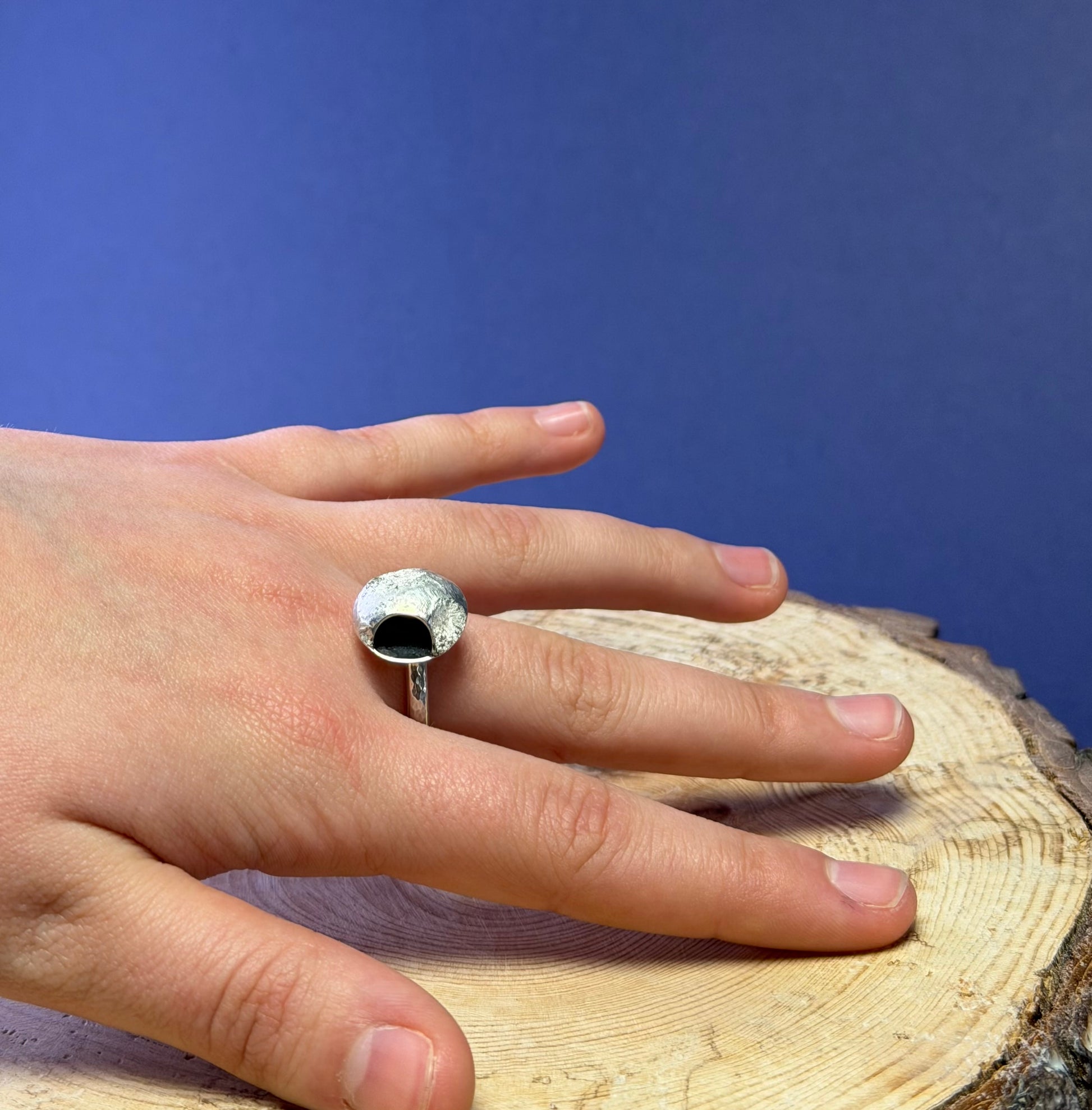 Hand wearing a silver ring with a moon design on a wooden surface with a blue background