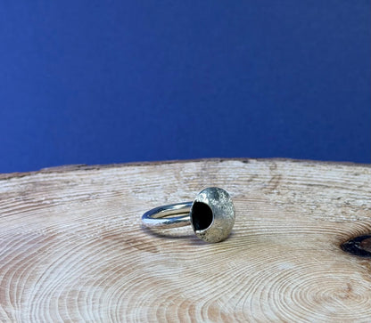Silver ring with a circular moon design on a wooden surface with a blue background