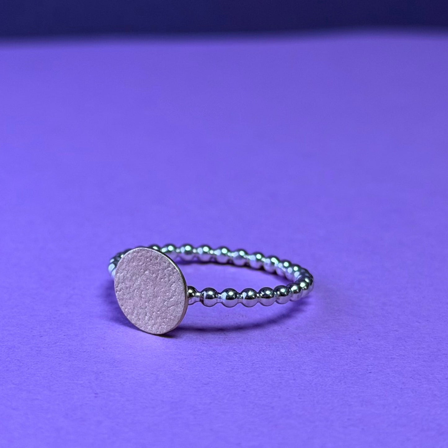 Silver ring with a round 9ct yellow disc on a purple background