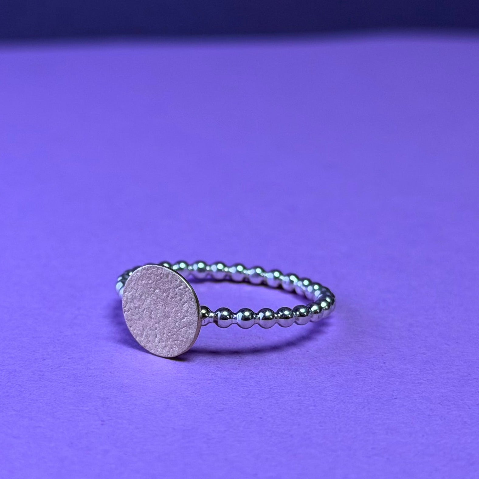 Silver ring with a round 9ct yellow disc on a purple background