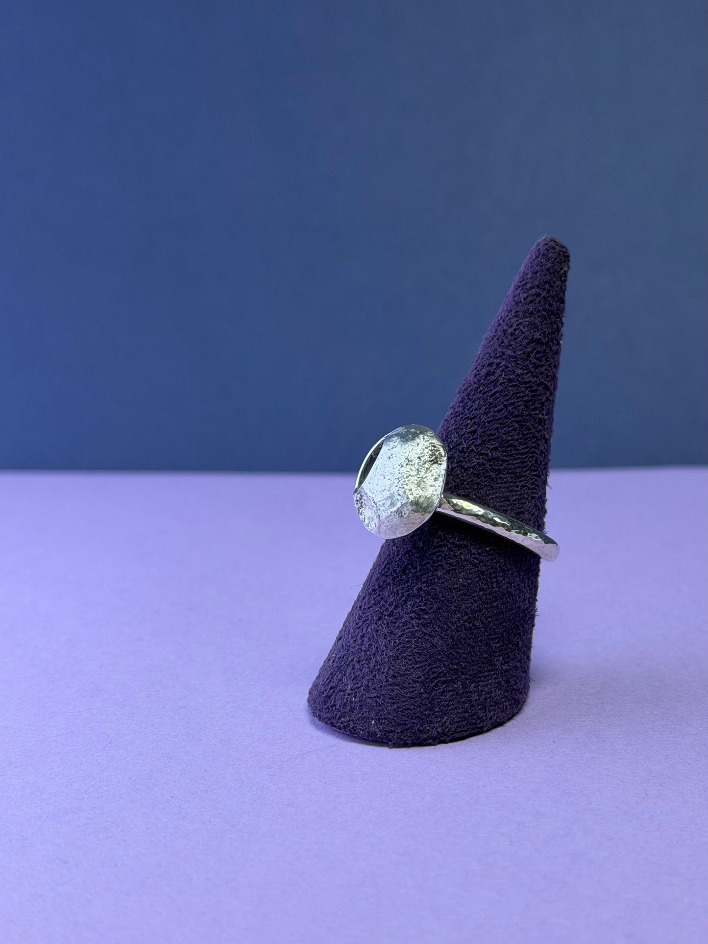 Silver ring with moon design on a purple cone-shaped stand against a blue background
