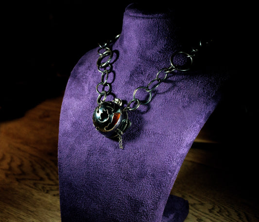Oxidised silver necklace with Phoenix cut out of front locket, with sunstone showing through a gap in the front, on a purple bust, dimly lit