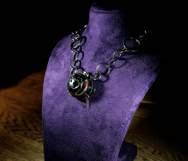 Oxidised silver necklace with Phoenix cut out of front locket, with sunstone showing through a gap in the front, on a purple bust, dimly lit