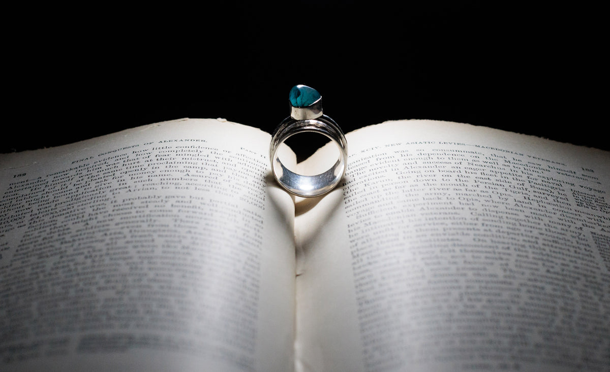 Sterling silver spinner ring with a green-blue stone, standing upright in the centre of an open book.