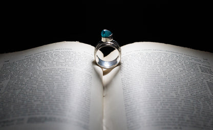 Sterling silver spinner ring with a green-blue stone, standing upright in the centre of an open book.
