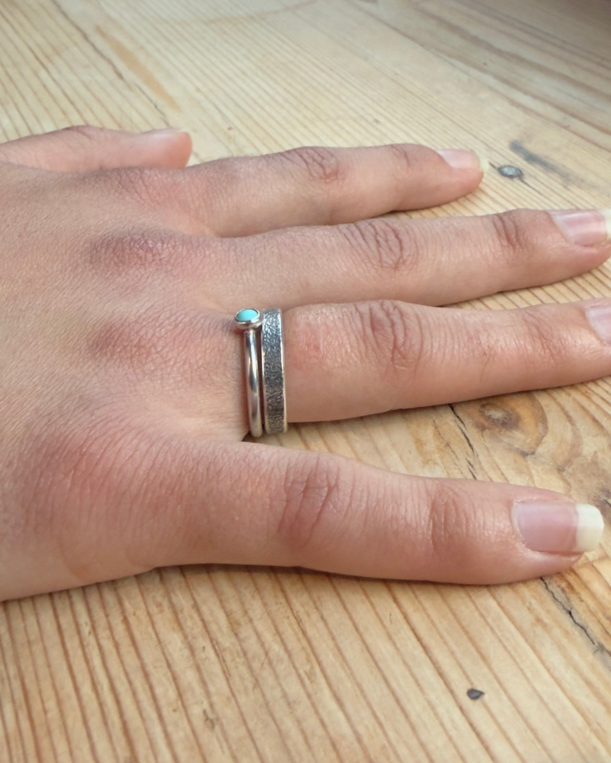  Angled view of a hand wearing the turquoise silver ring stacked with a textured silver band.