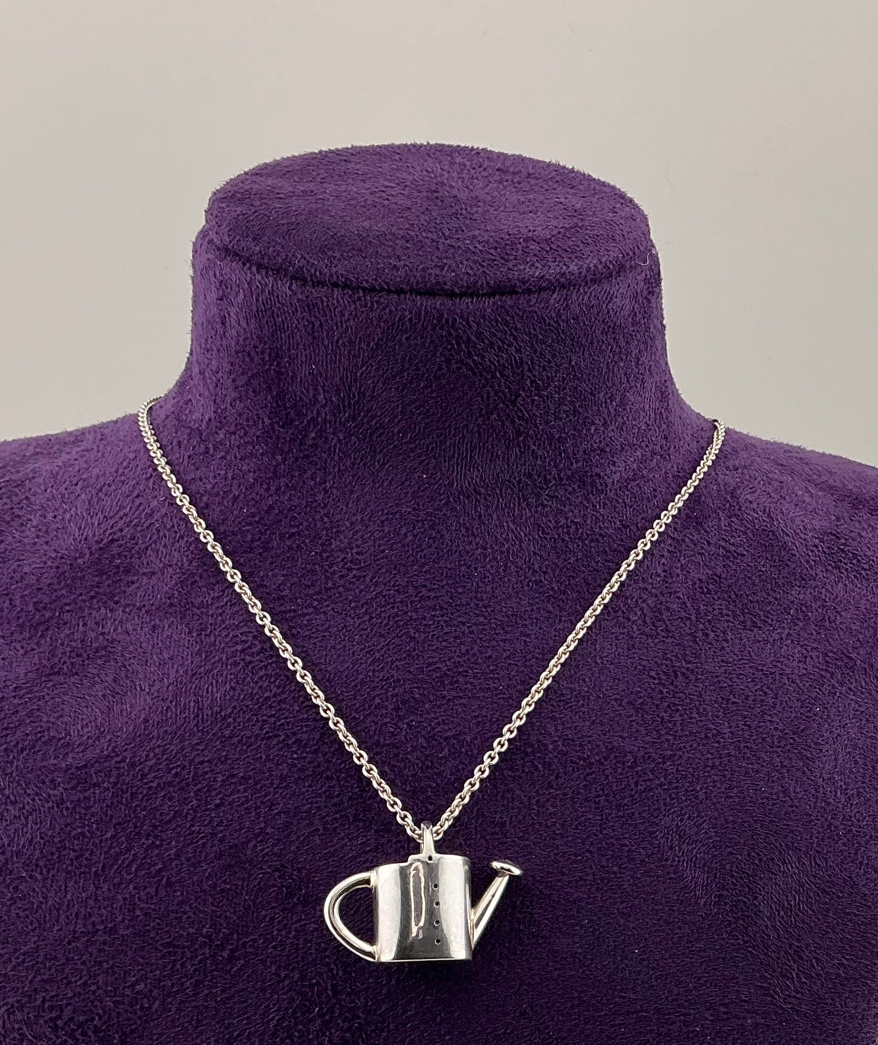 Watering can pendant on a chain displayed on a purple mannequin bust.