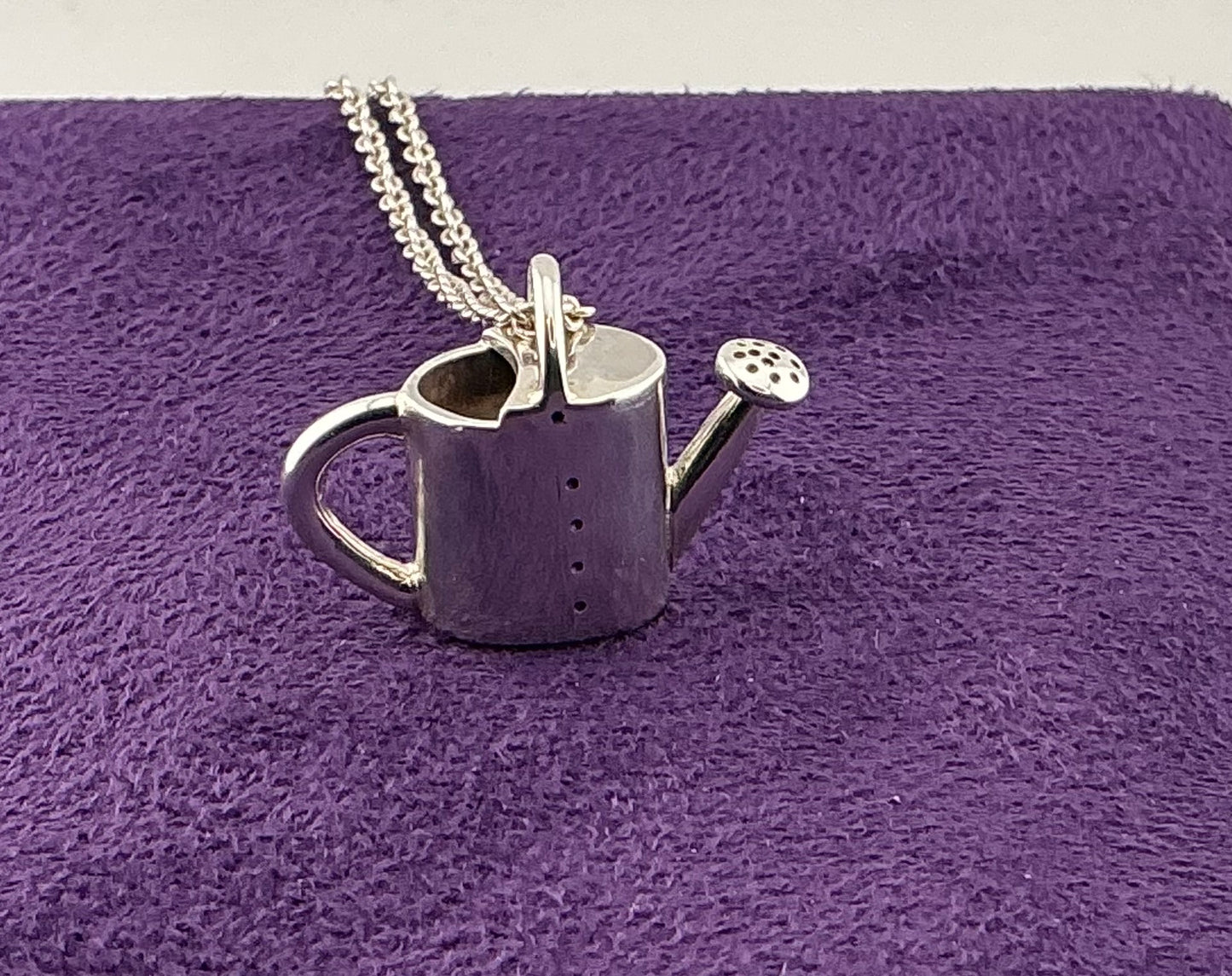 Silver watering can pendant on a chain against a purple textured background