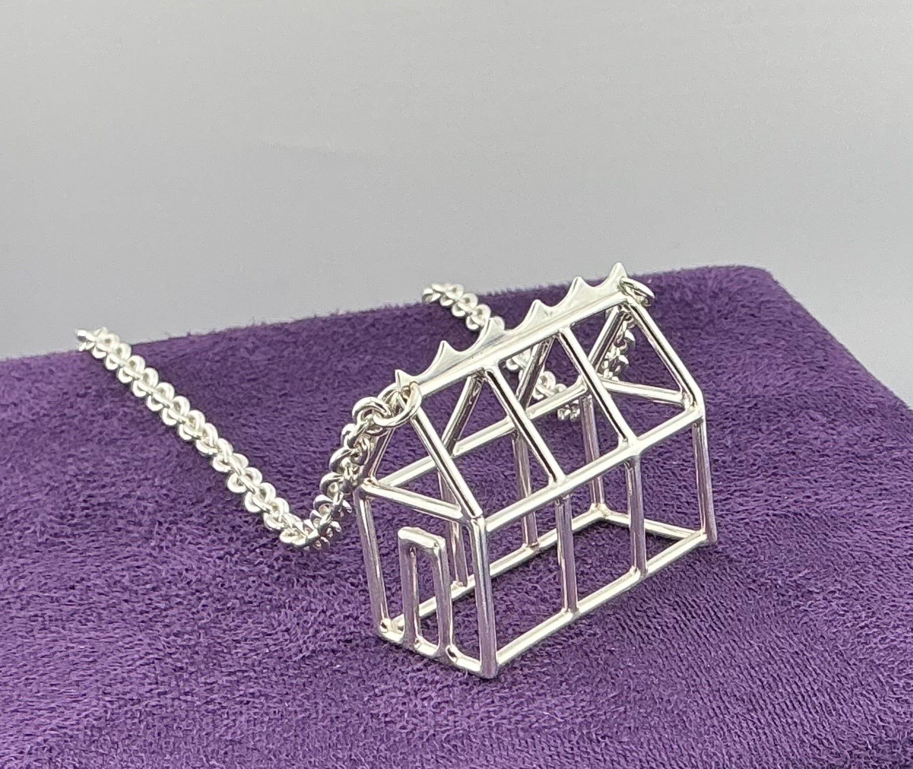 Silver geometric Greenhouse necklace on a purple surface with a grey background