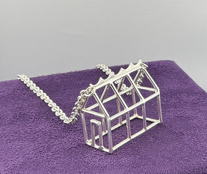 Silver geometric Greenhouse necklace on a purple surface with a grey background