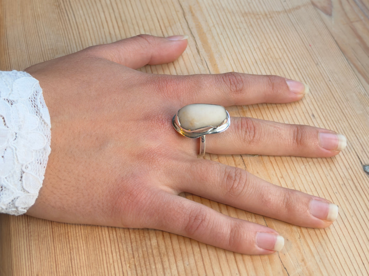Top view of a beach pebble ring worn on a hand, showing the smooth cream-coloured stone framed by an organic sterling silver setting.