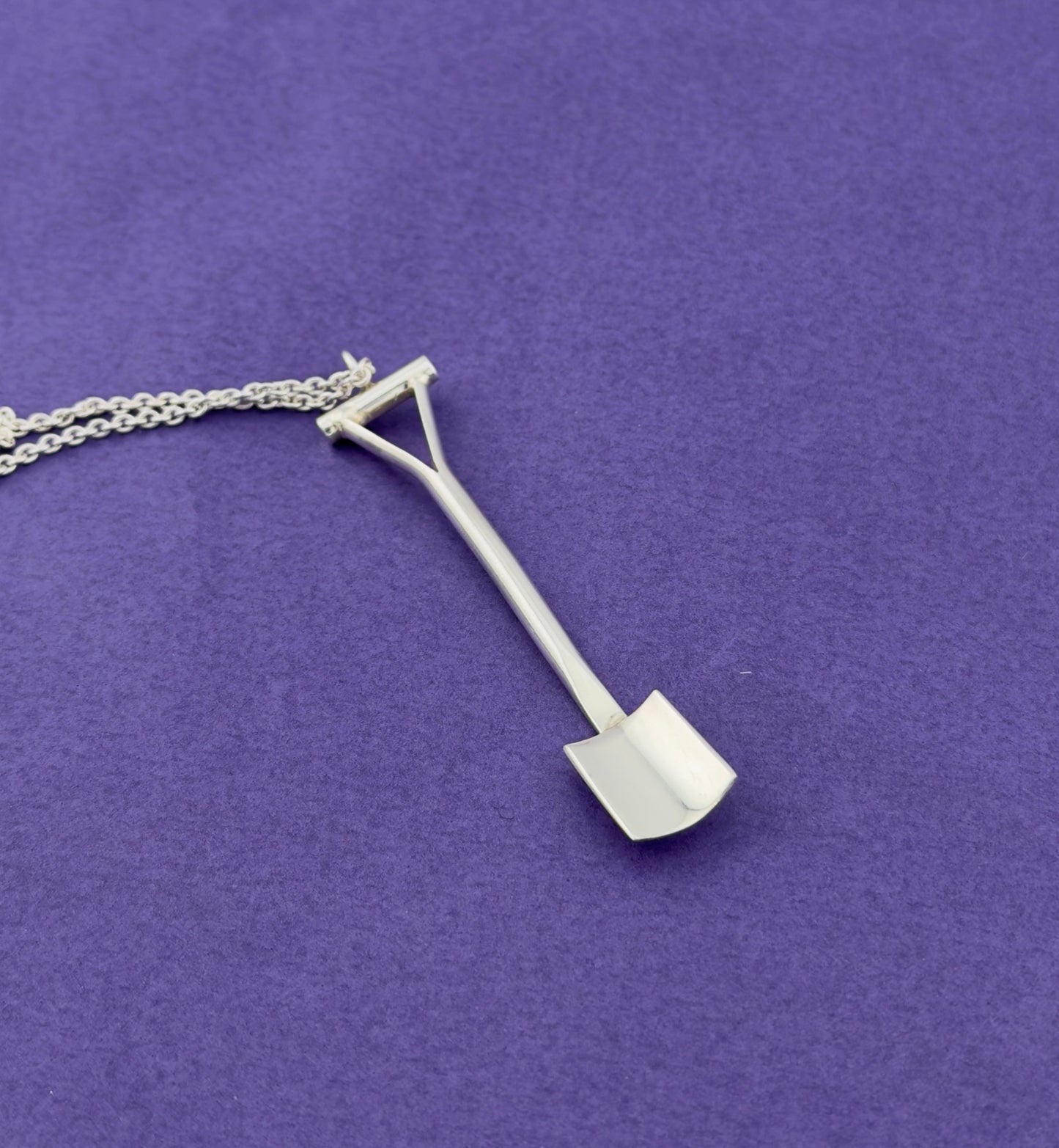 Silver spade shaped pendant on a chain against a purple background