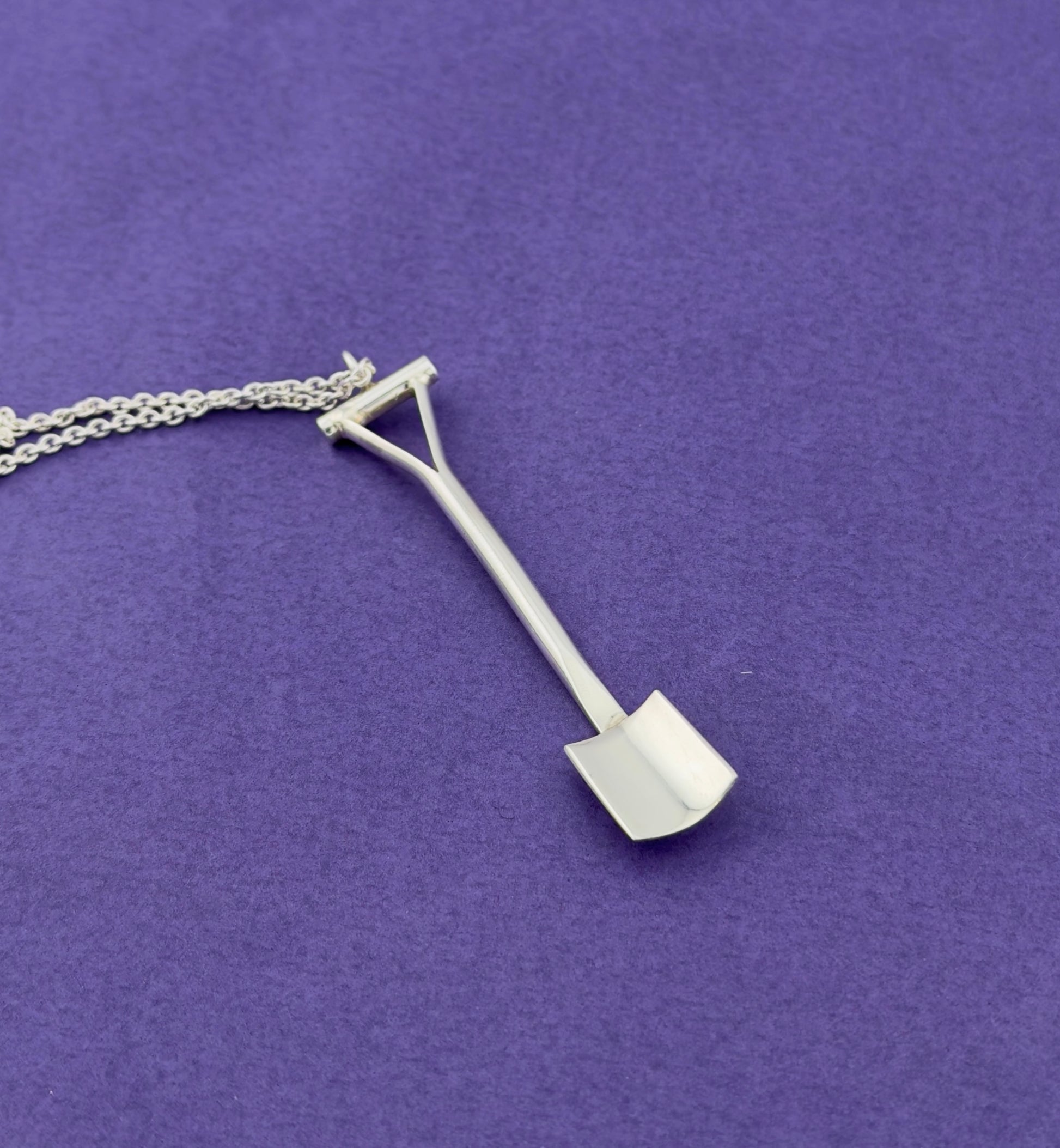 Silver spade shaped pendant on a chain against a purple background