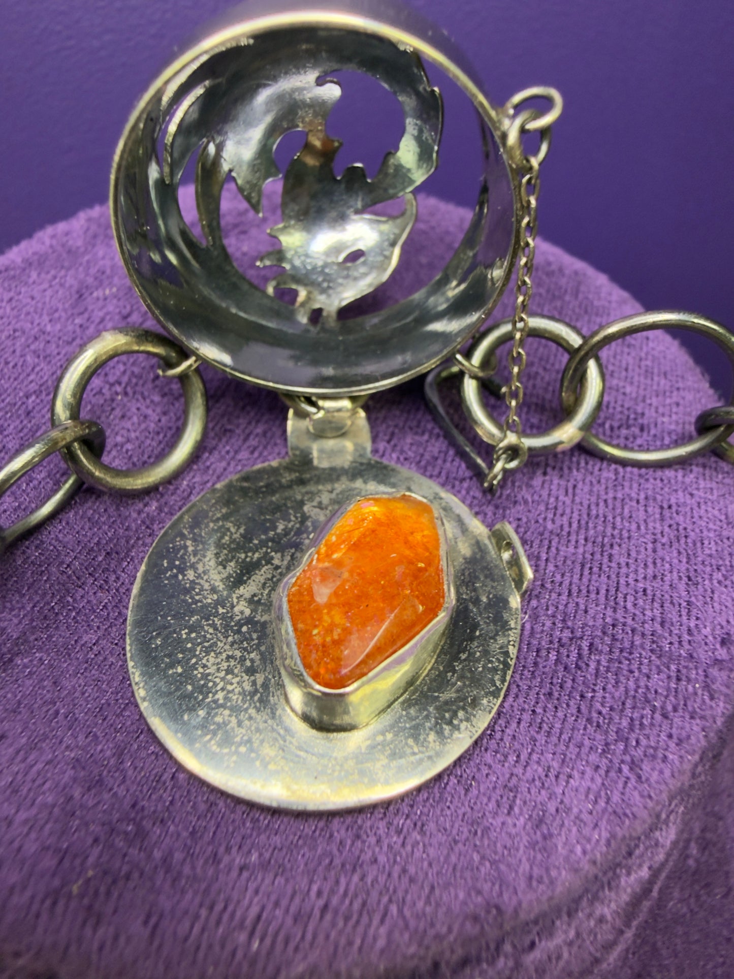 Silver pendant with an orange stone on a purple fabric background