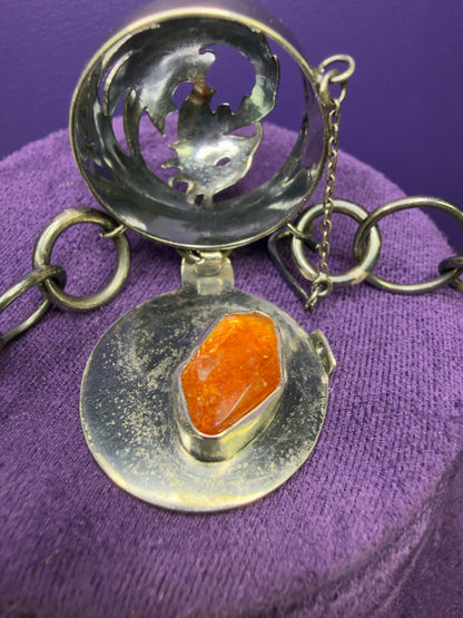 Silver pendant with an orange stone on a purple fabric background