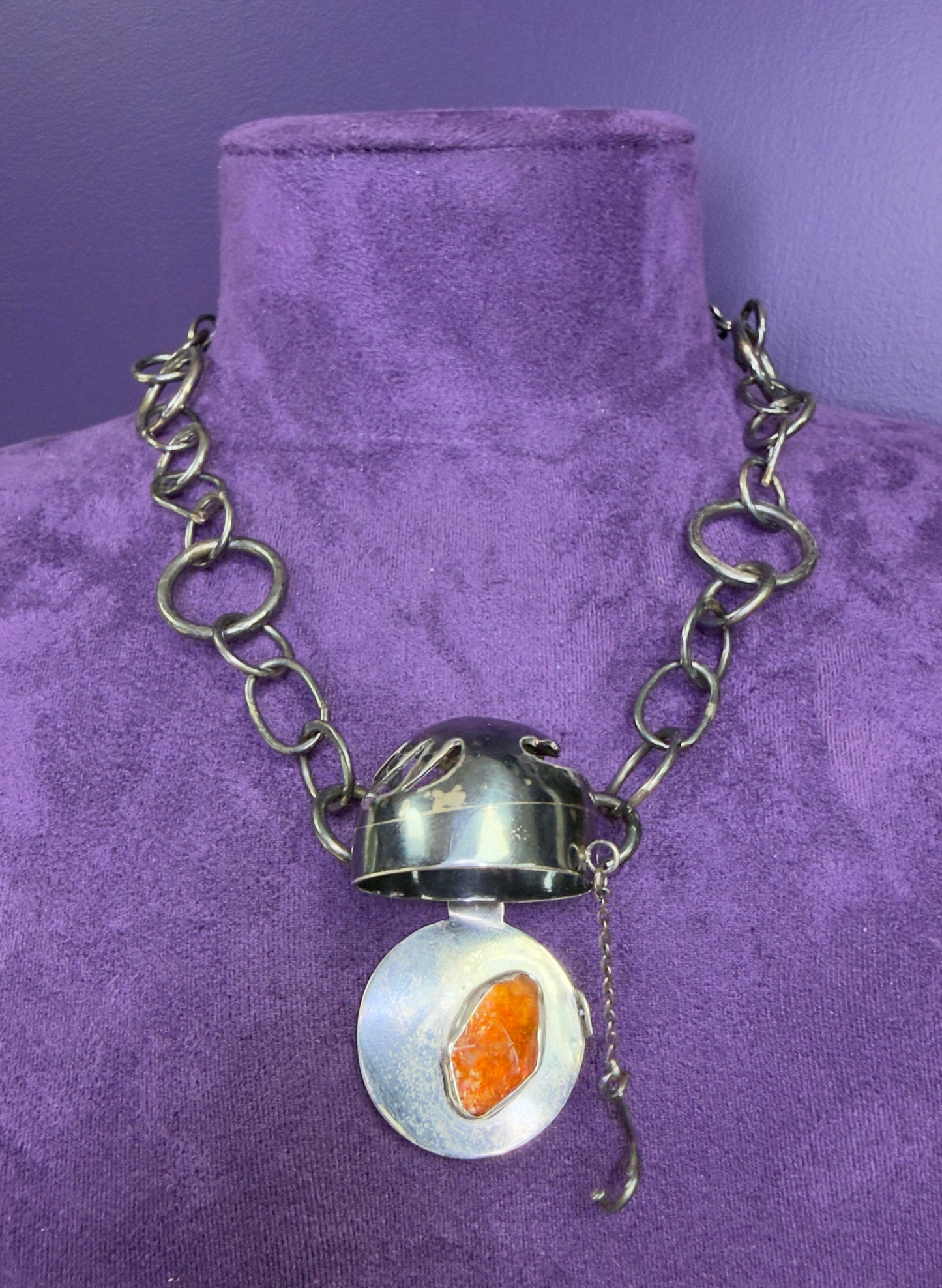 Silver necklace with a round pendant featuring an orange stone on a purple velvet background
