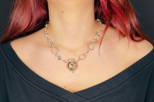 Person wearing a silver chain necklace with a circular pendant.