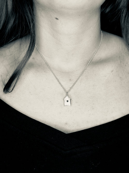 Necklace with a small birdhouse pendant worn by a person
