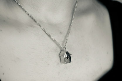 Silver necklace with a birdhouse pendant on a neutral background