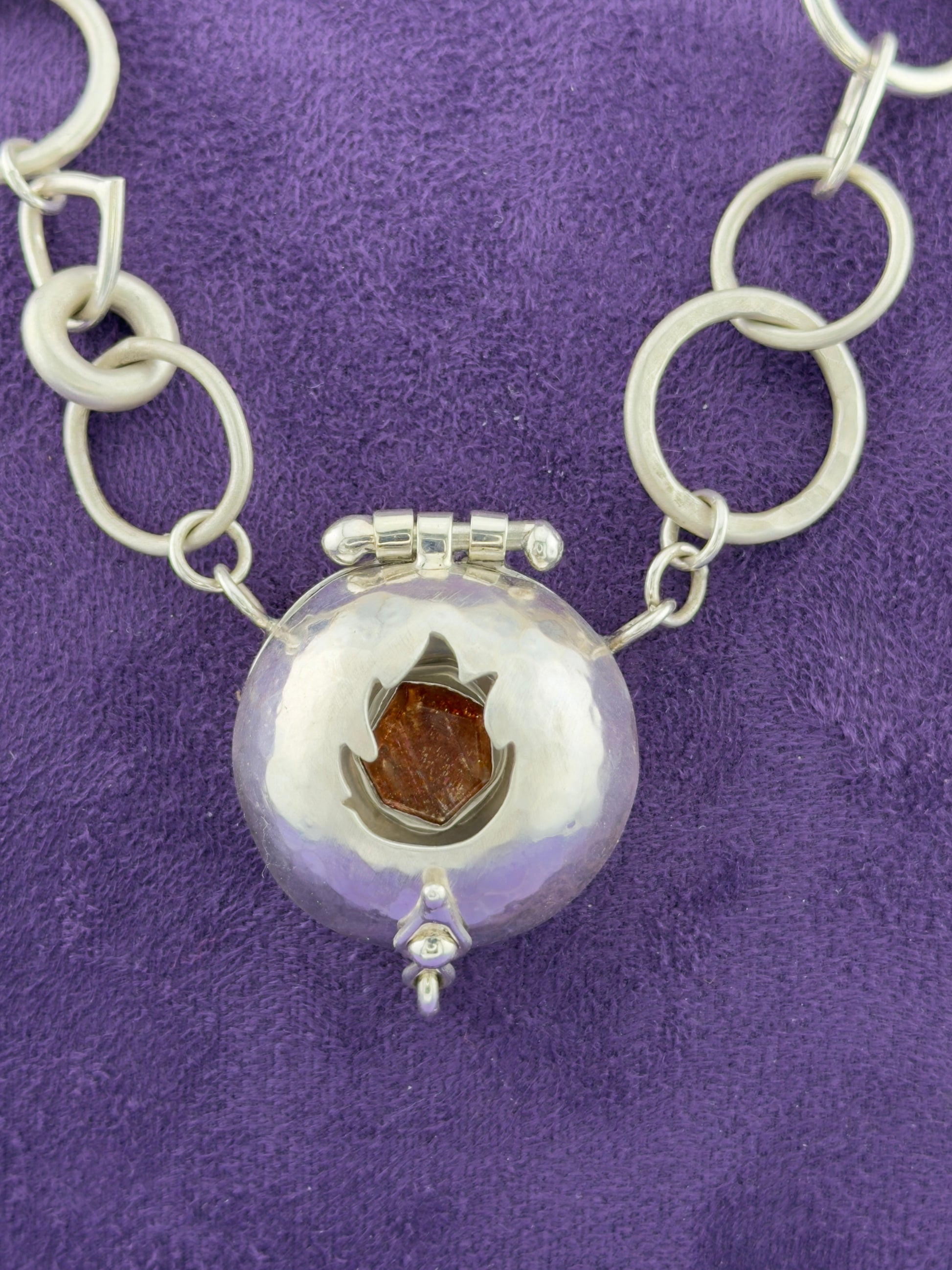 Silver necklace with a round pendant on a purple background