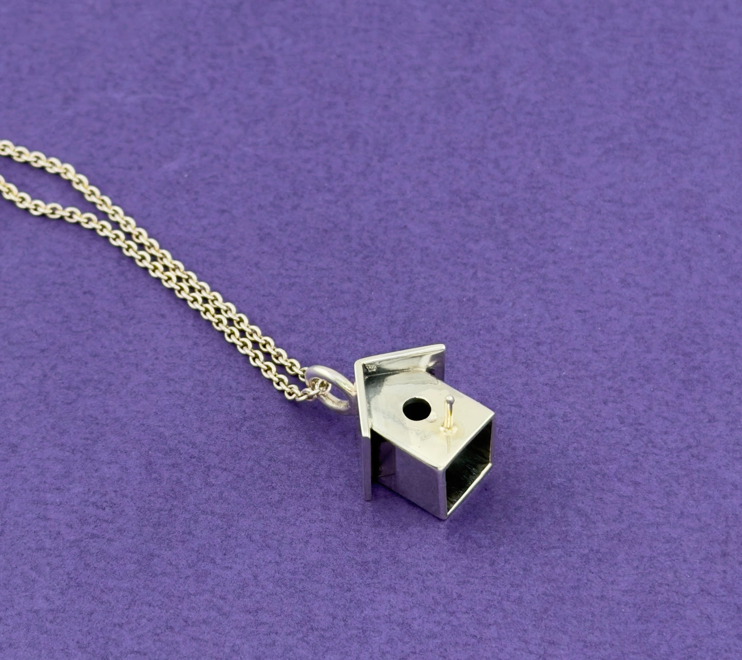 Silver birdhouse pendant necklace on a purple background
