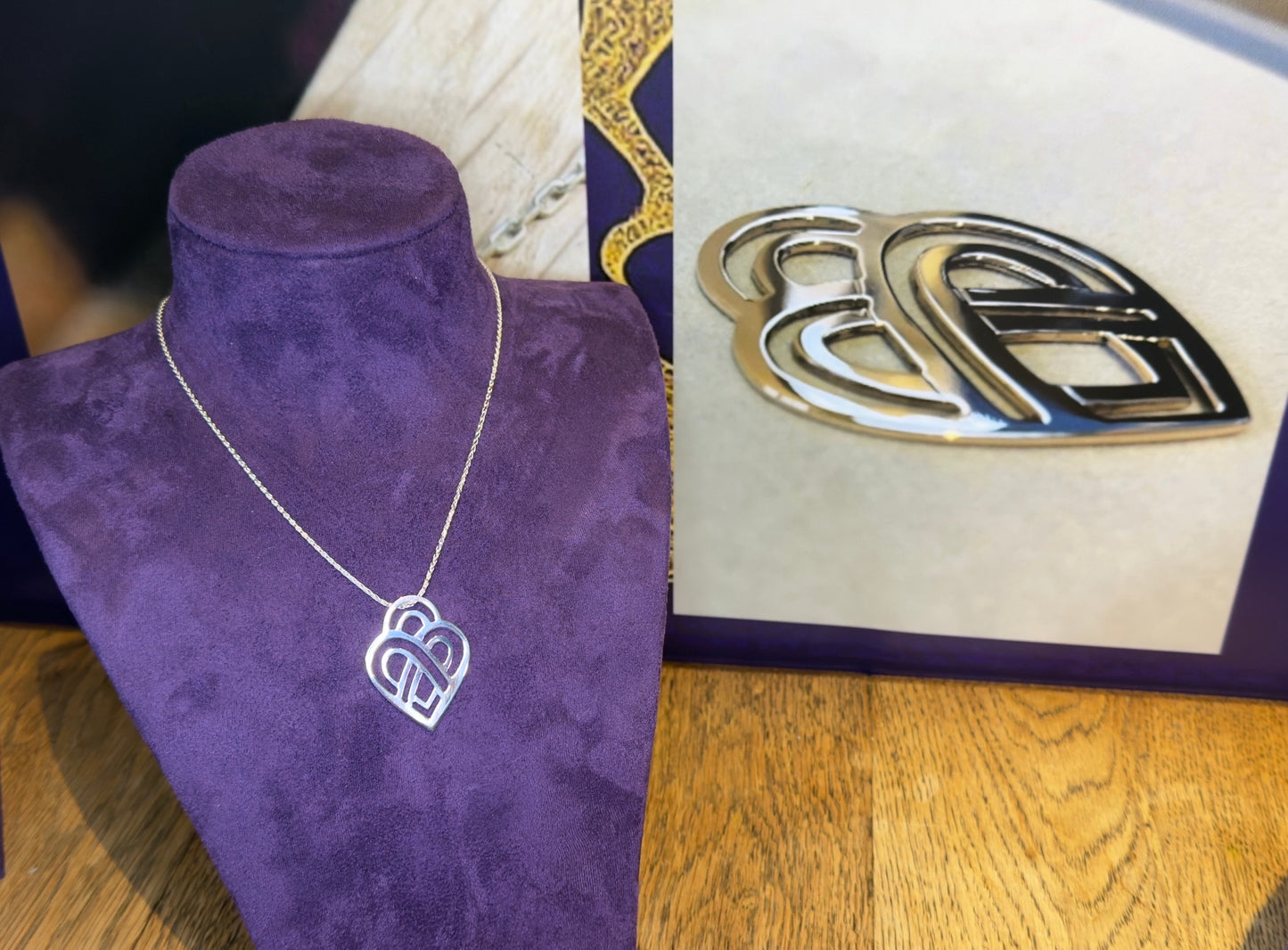 Silver necklace with a heart pendant on a purple stand, next to a photo of a gold version on a white background.