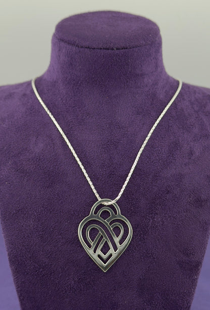 Silver necklace with a heart-shaped pendant on a purple velvet stand.