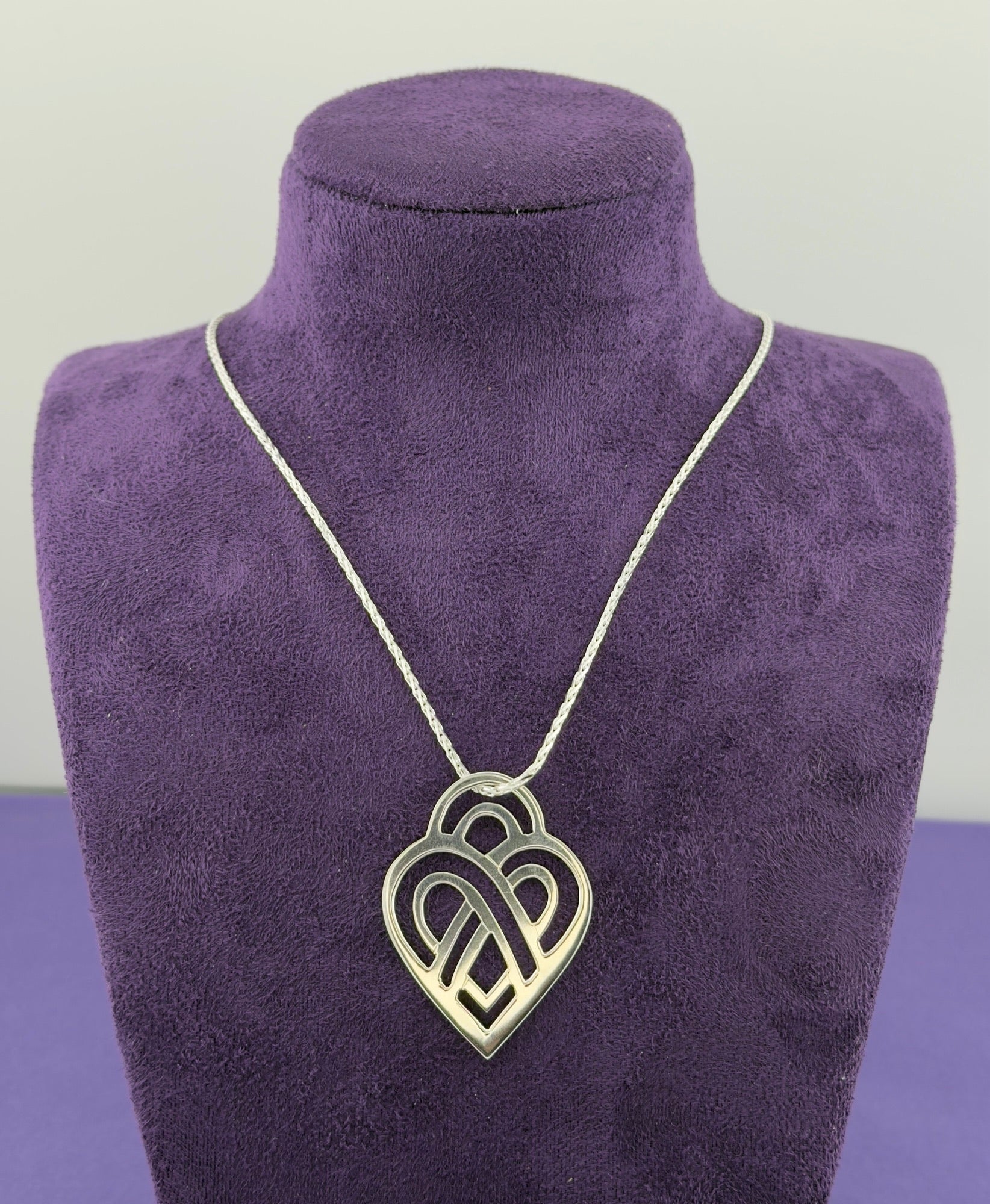 Necklace with a heart-shaped pendant on a purple mannequin bust.