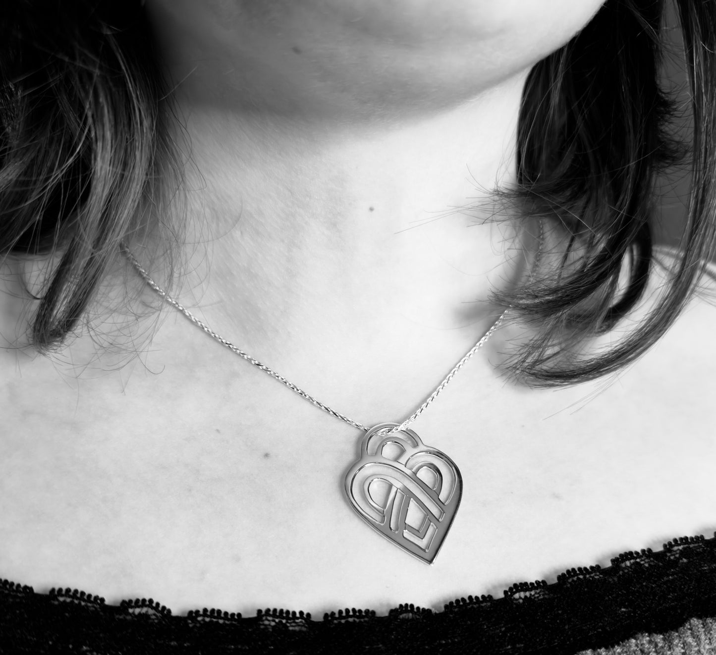 Person wearing a necklace with a heart-shaped pendant featuring a design.