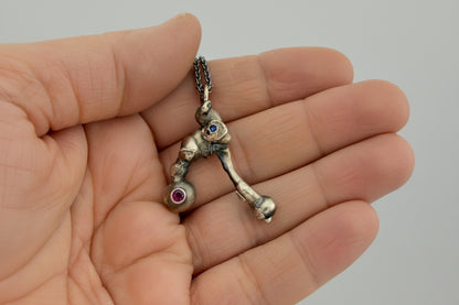 Silver skeleton key necklace with a pink/red gemstone held in a hand against a neutral background