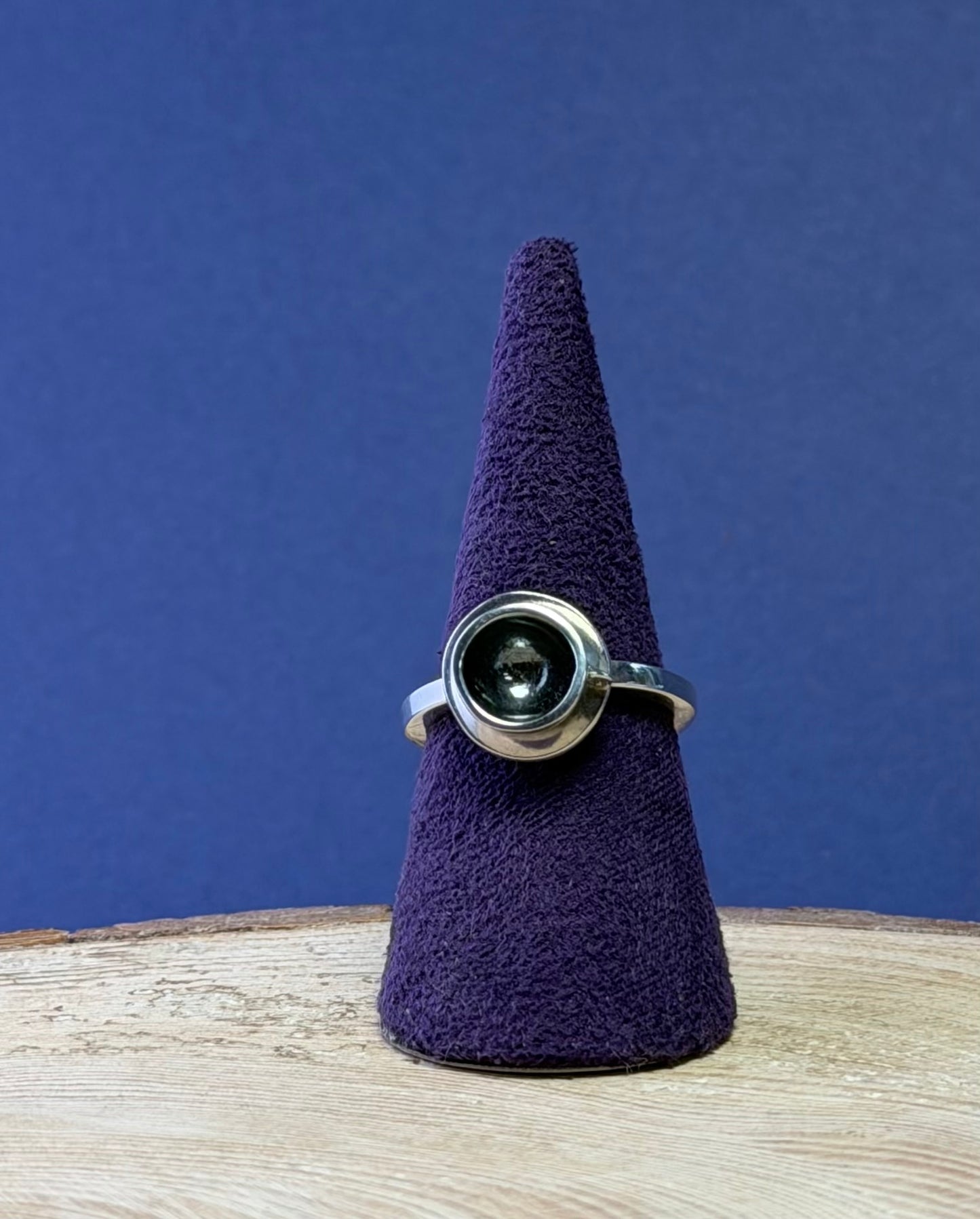 Silver teacup ring with a central gemstone on a purple cone against a blue background