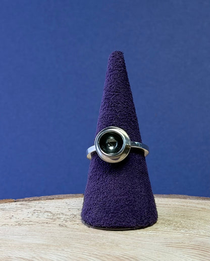 Silver teacup ring with a central gemstone on a purple cone against a blue background