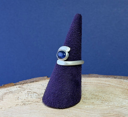 Purple felted ring holder with a ring on a wooden surface against a blue background