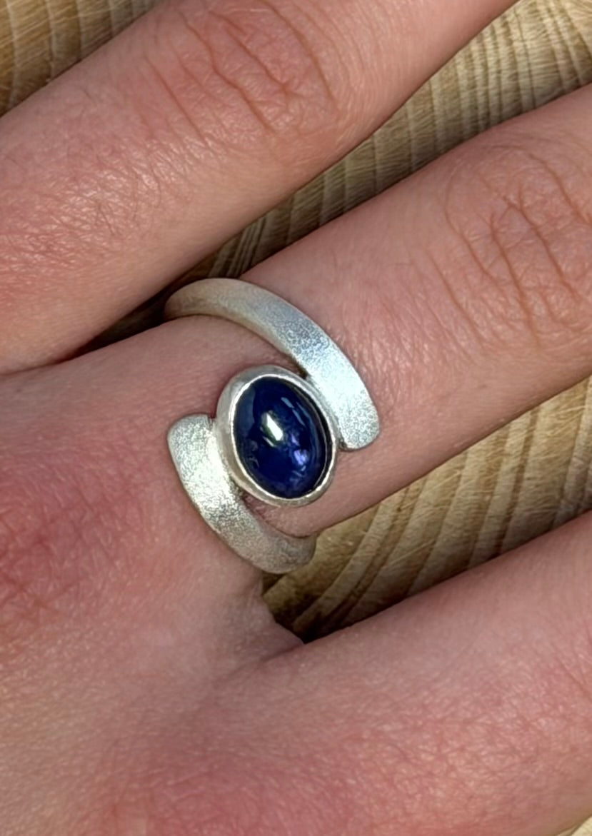 Silver ring with a blue purple 
gemstone on a finger
