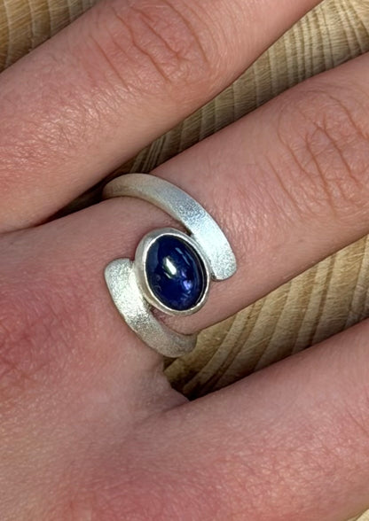 Silver ring with a blue purple 
gemstone on a finger