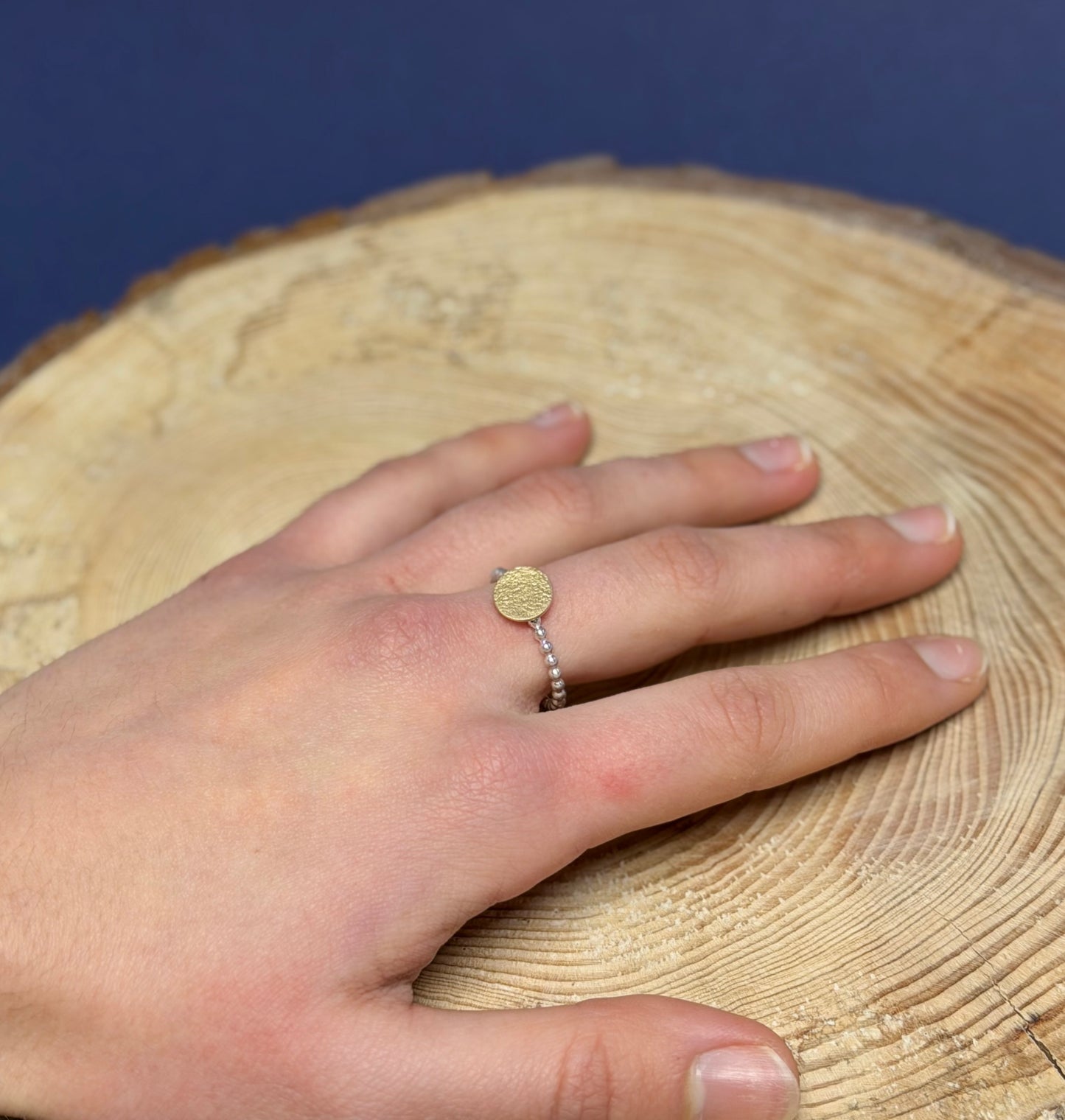 Hand wearing a gold and silver  ring on a wooden surface with a blue background