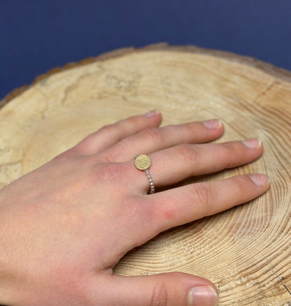 Hand wearing a gold and silver  ring on a wooden surface with a blue background