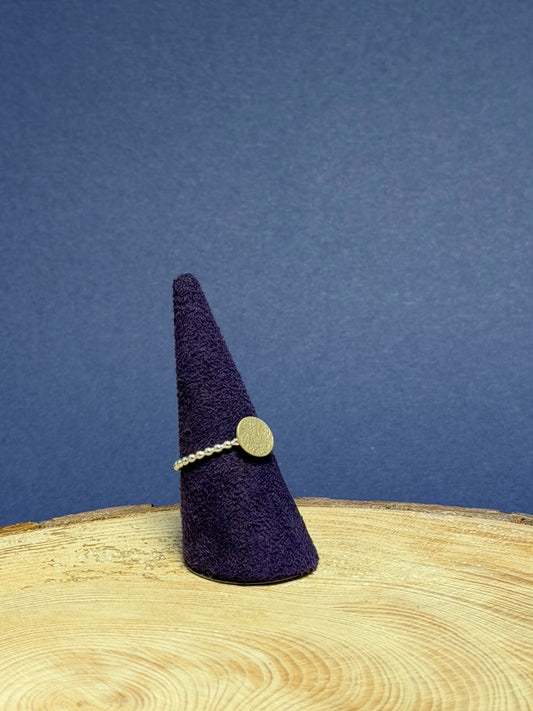 Purple felt cone with a gold and silver ring on a wooden surface against a blue background