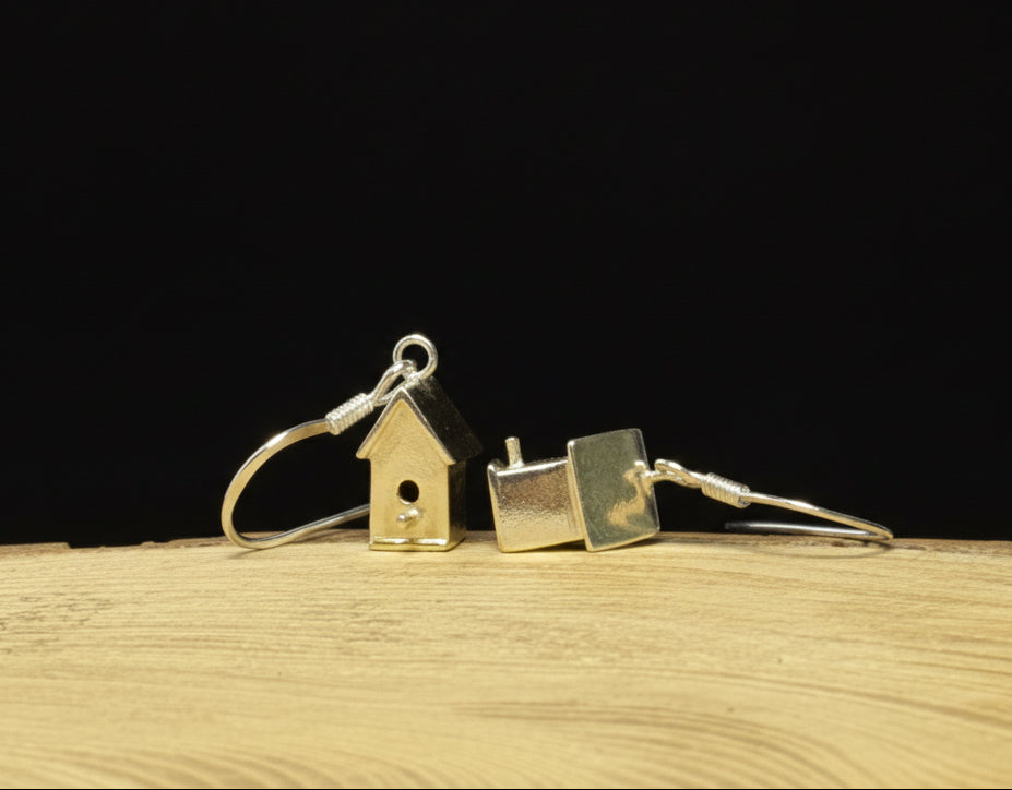 Silver birdhouse shaped earrings on a wooden surface with a black background