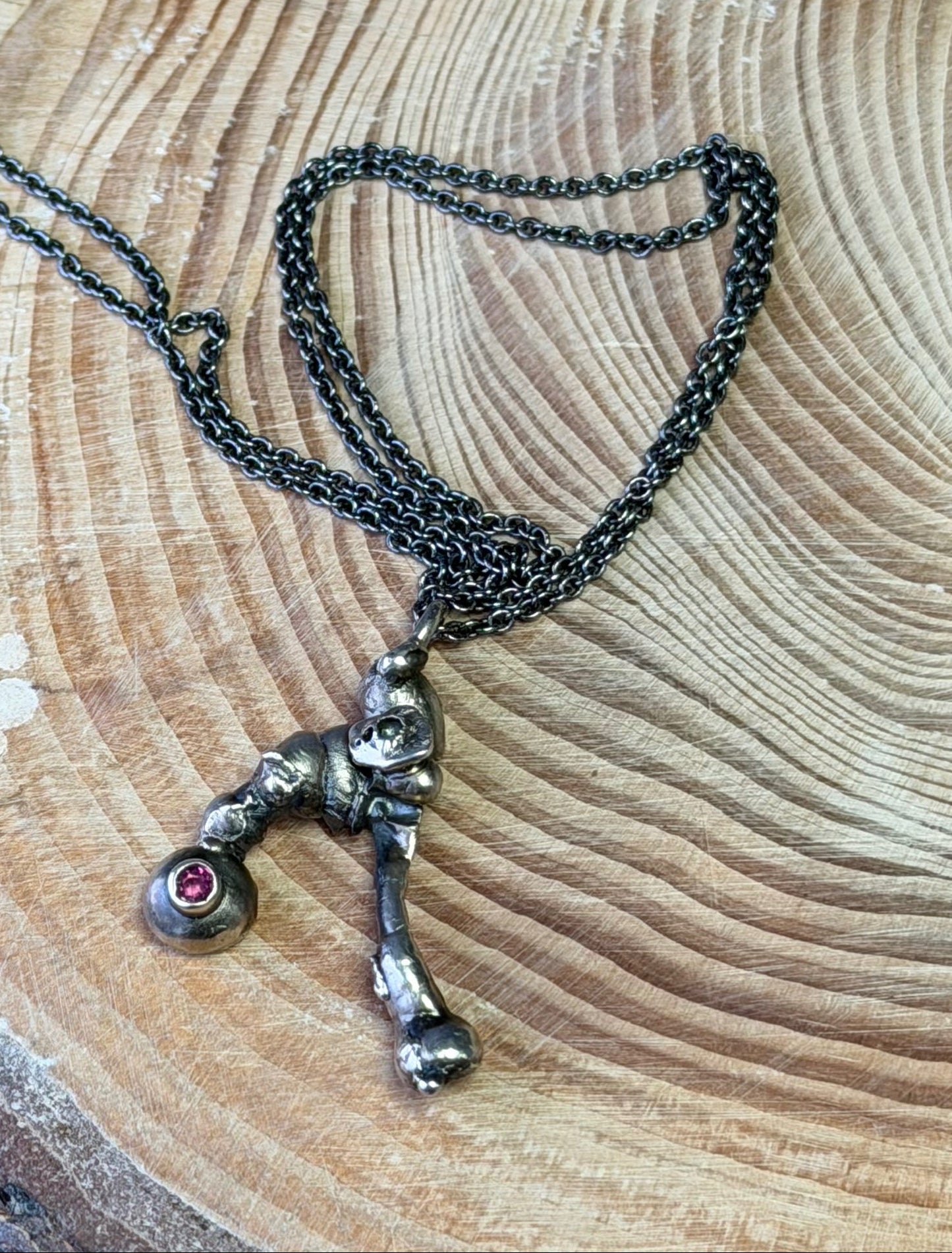 Necklace with a molten pendant set with a Rhodolite Garnet on a wooden log against a blue background