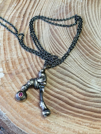 Necklace with a molten pendant set with a Rhodolite Garnet on a wooden log against a blue background