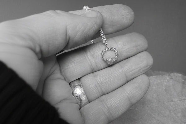 Beaded silver necklace circular pendant on chain, held in a hand