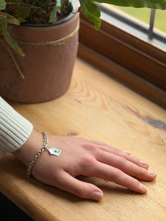 Hand resting on a wooden window sill, with Birdhouse bracelet on wrist