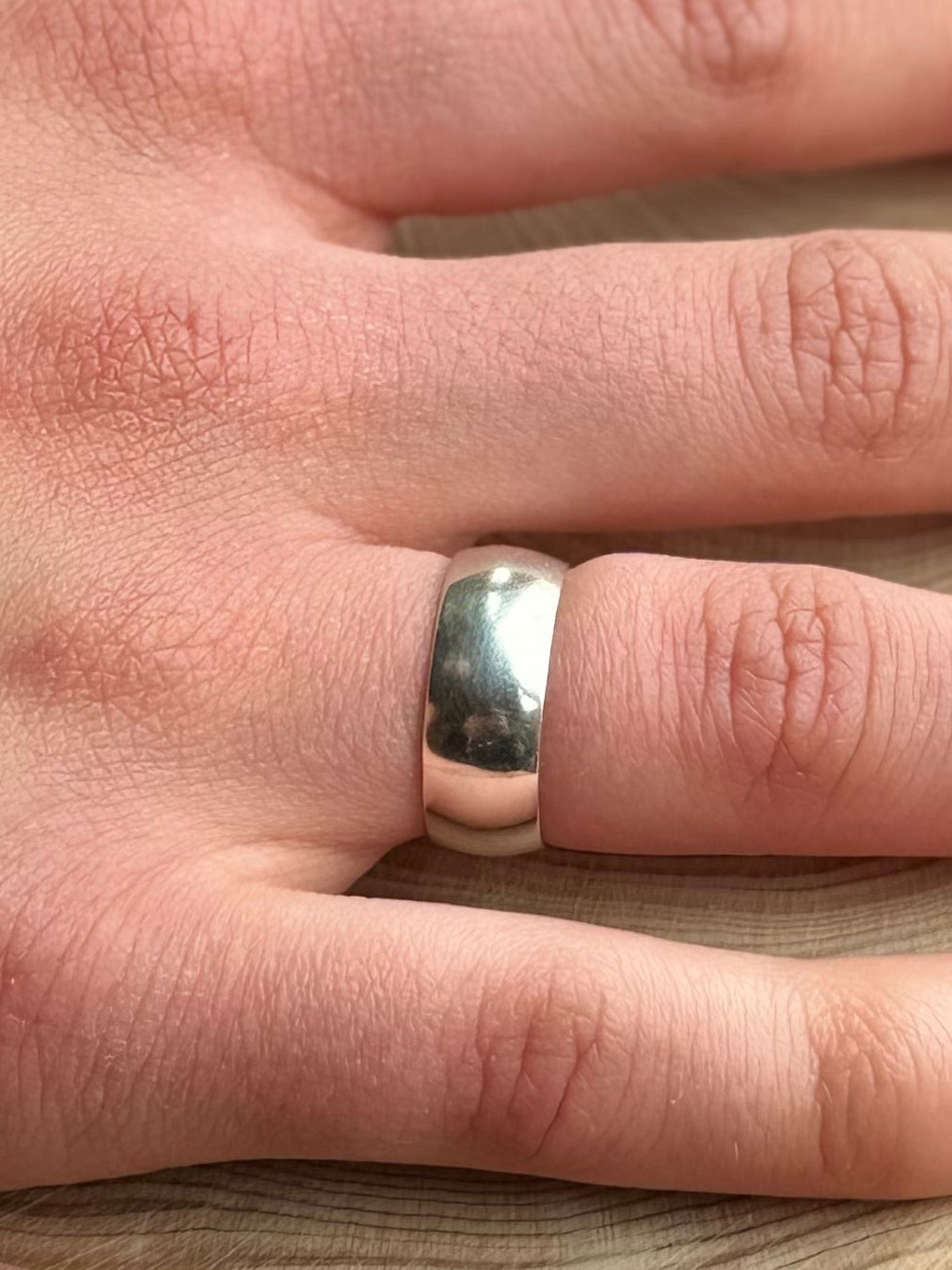 Wide silver ring band,D-shaped profile, on hand resting on wood