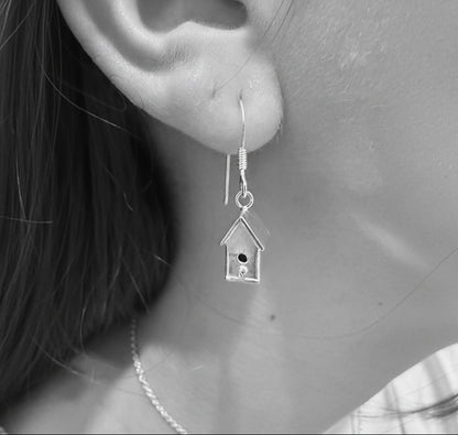 Silver birdhouse earring worn on an ear